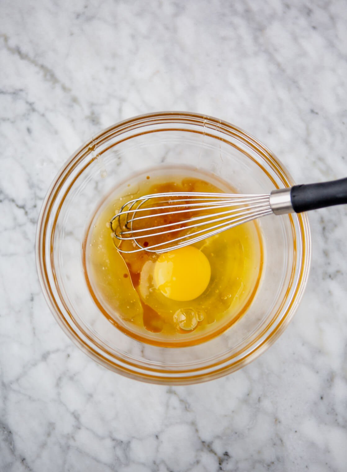 Egg and vanilla in a glass bowl with a whisk.
