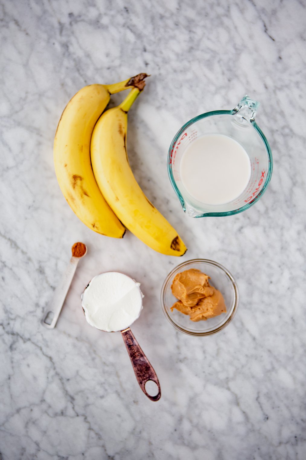 Peanut butter banana smoothie bowl ingredients on a grey and white marble surface.