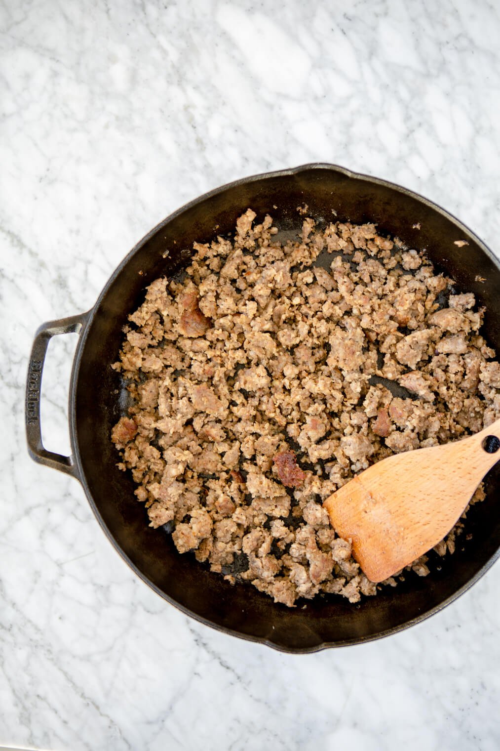 Browned breakfast sausage in a cast iron skillet with wooden spatula.