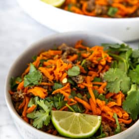 Bowl of shredded carrot breakfast hash garnished with lime and cilantro.