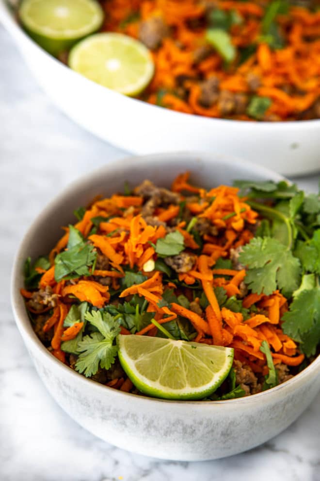 Bowl of shredded carrot breakfast hash garnished with lime and cilantro.