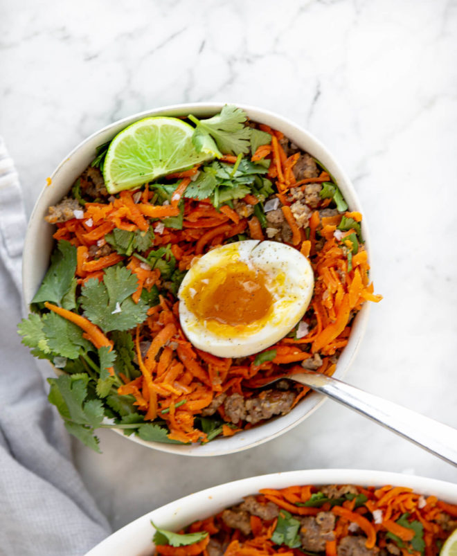Bowl of shredded carrot breakfast hash garnished with lime, cilantro, and soft boiled egg.