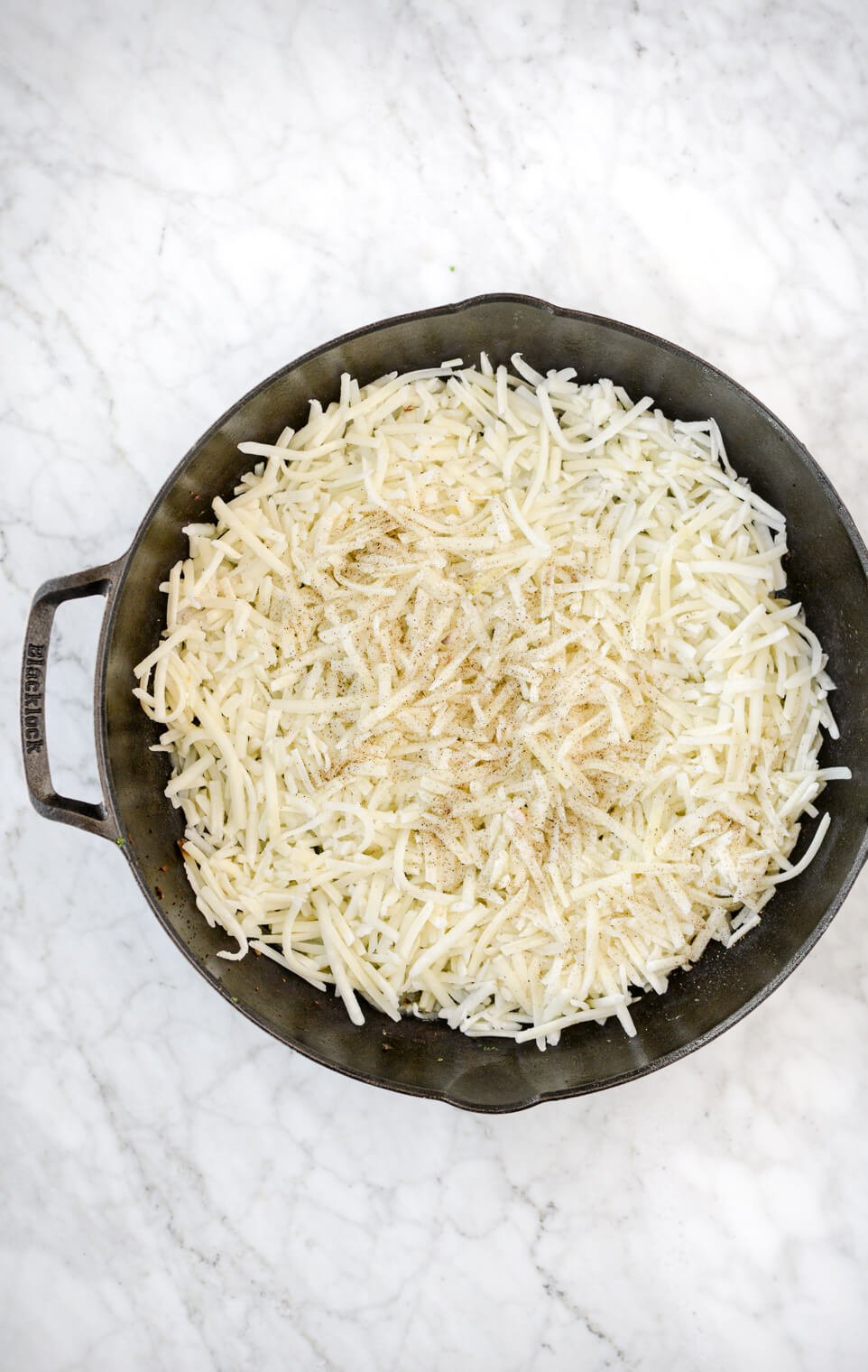 Hash browns spread across the bottom of a cast iron skillet.