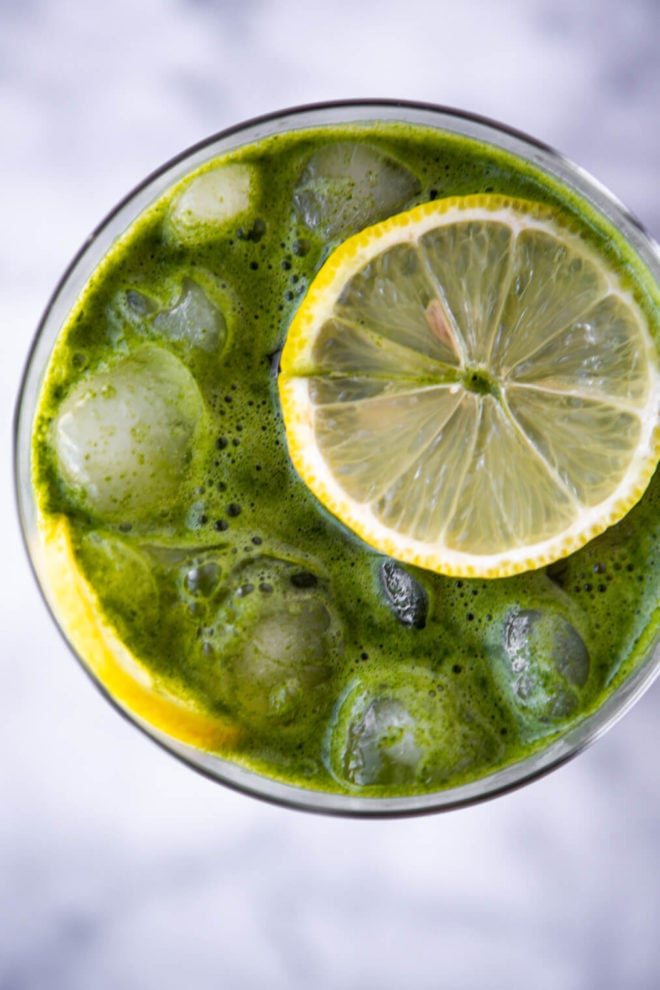 Top view of green juice in glass topped with lemon slice.