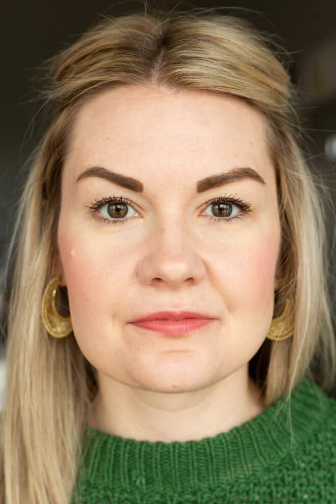 Headshot of Lauren in a Kelly green sweater not smiling wearing Cover Girl mascara.