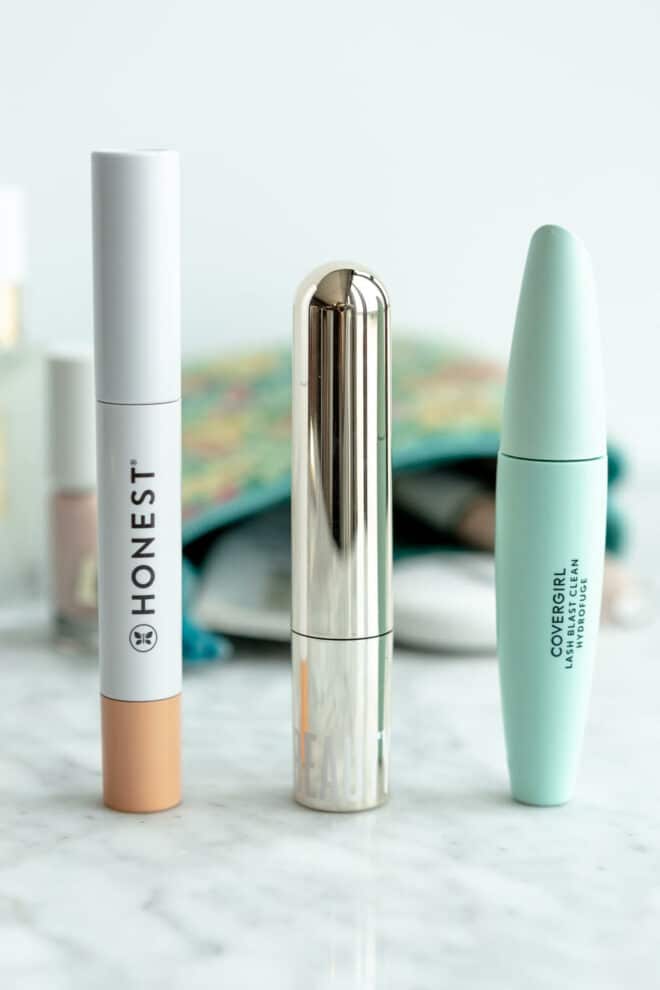 Three mascaras lined up on a grey and white marble surface with a makeup bag in the background.