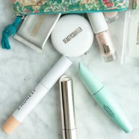 Top down view of three mascara tubes on a gray and white marble surface with a turquoise floral make up bag.