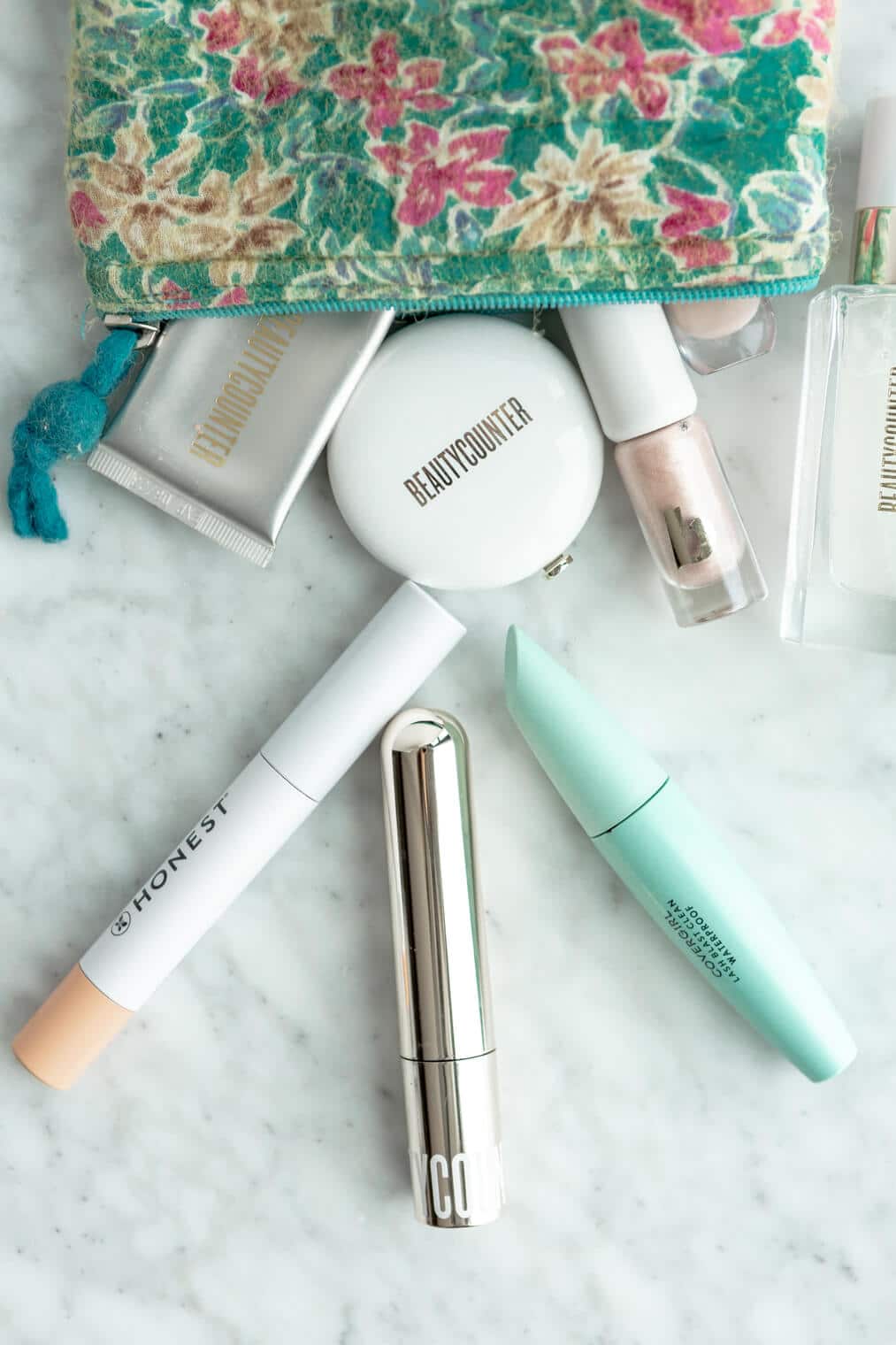 Top down view of three mascara tubes on a gray and white marble surface with a turquoise floral make up bag.