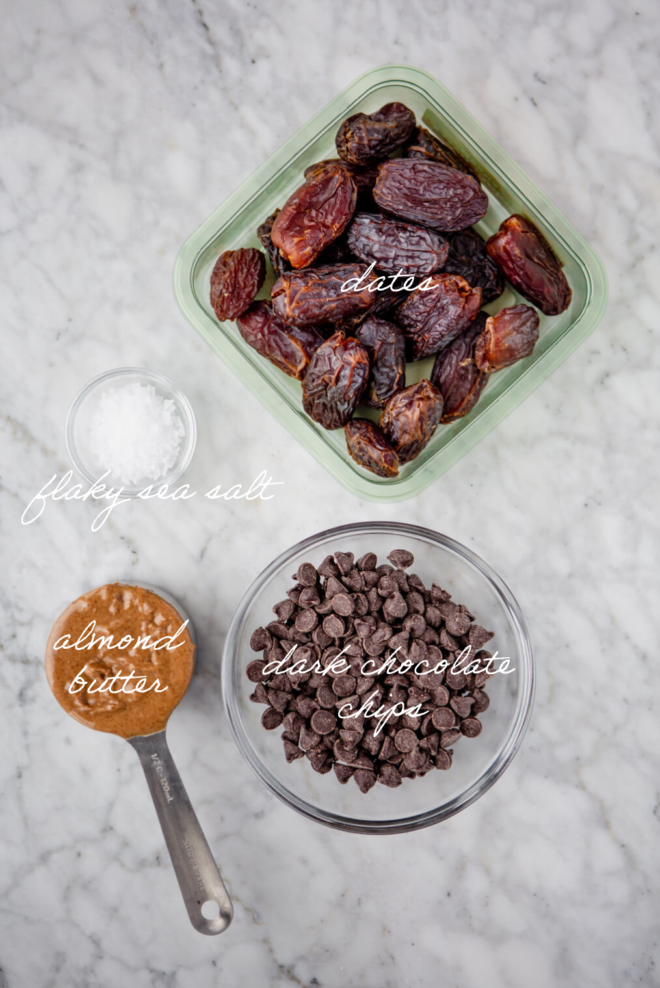 Chocolate Almond Butter Dates ingredients on a marble surface with labels over ingredients in white cursive letters.