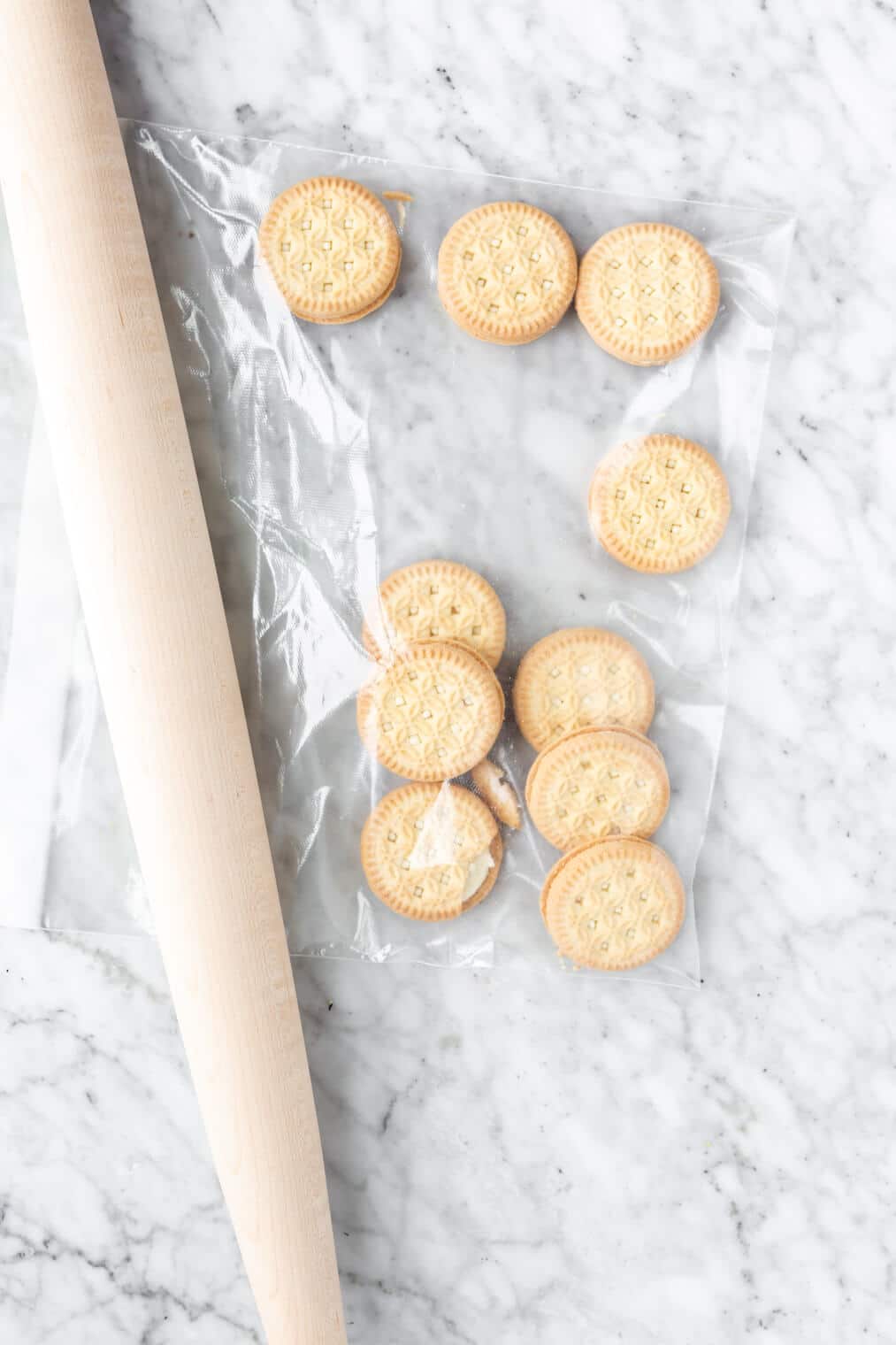 Rolling pin next to a plastic bag full of vanilla, cream filled cookies.