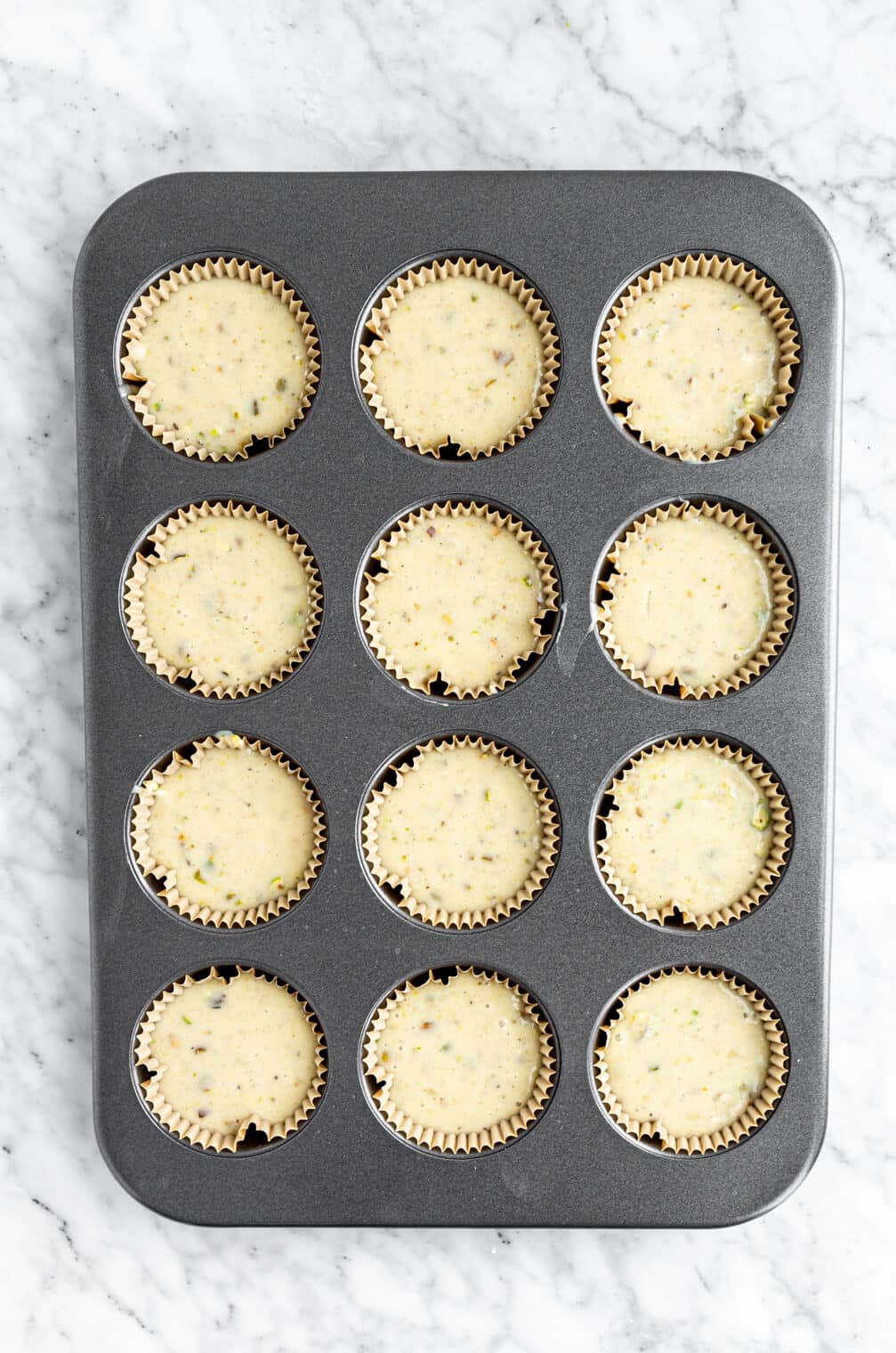 Muffin batter in a cupcake baking tin lined with muffin liners.