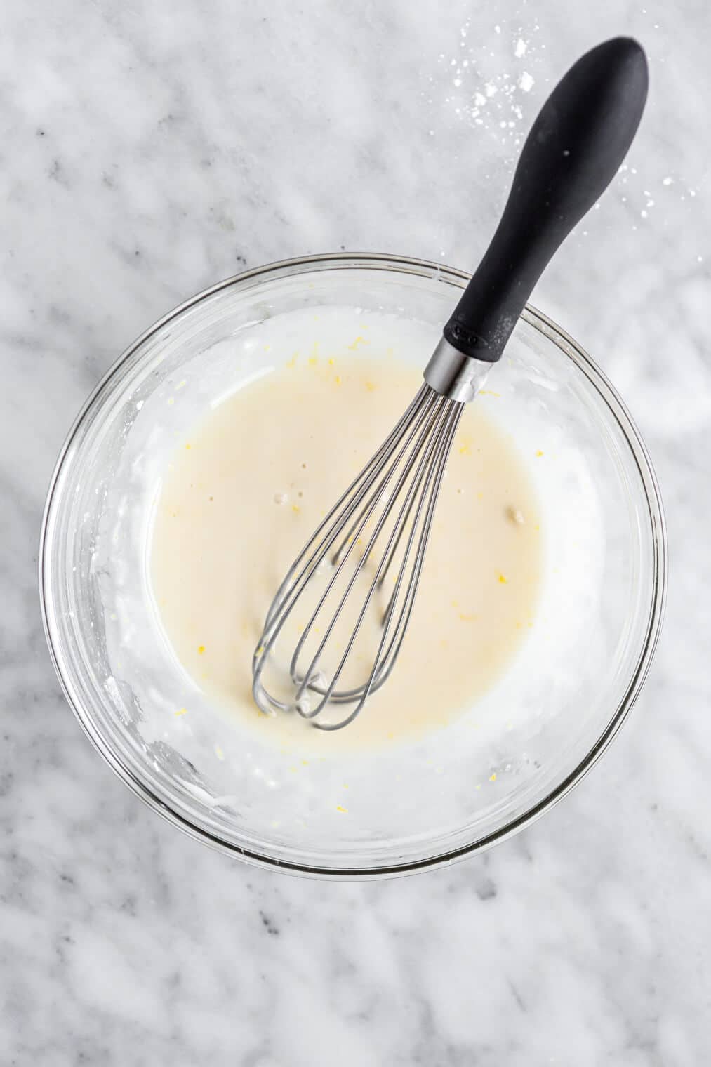 White glaze in a glass mixing bowl with a whisk.