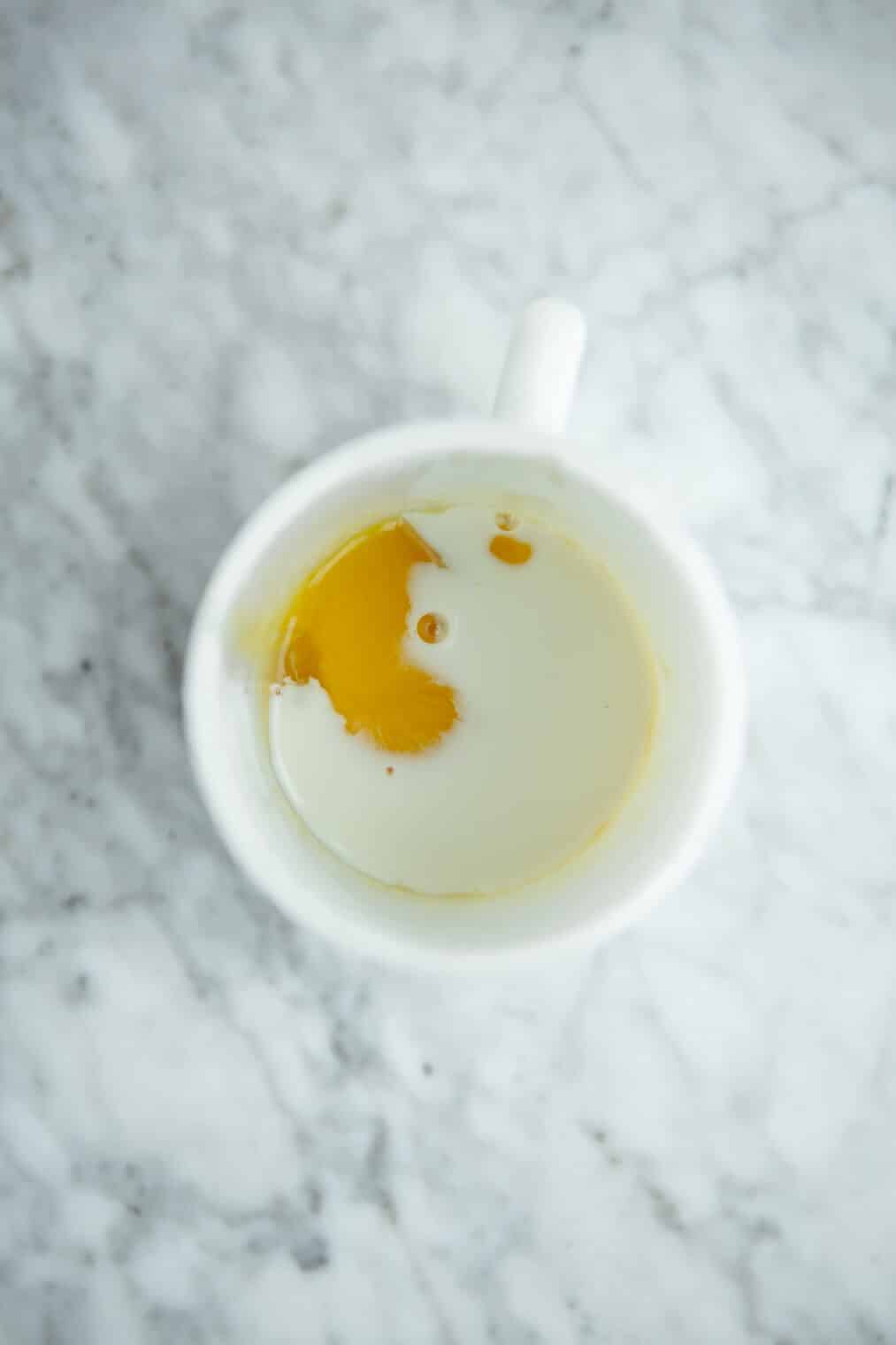 Top down view of white mug with milk and egg added to cookie ingredients.