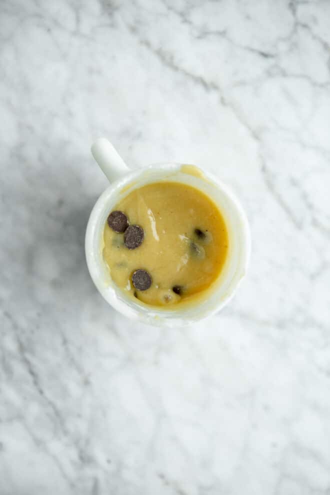 Mug cake cookie dough ingredients in a white coffee mug on a grey and white marble surface.