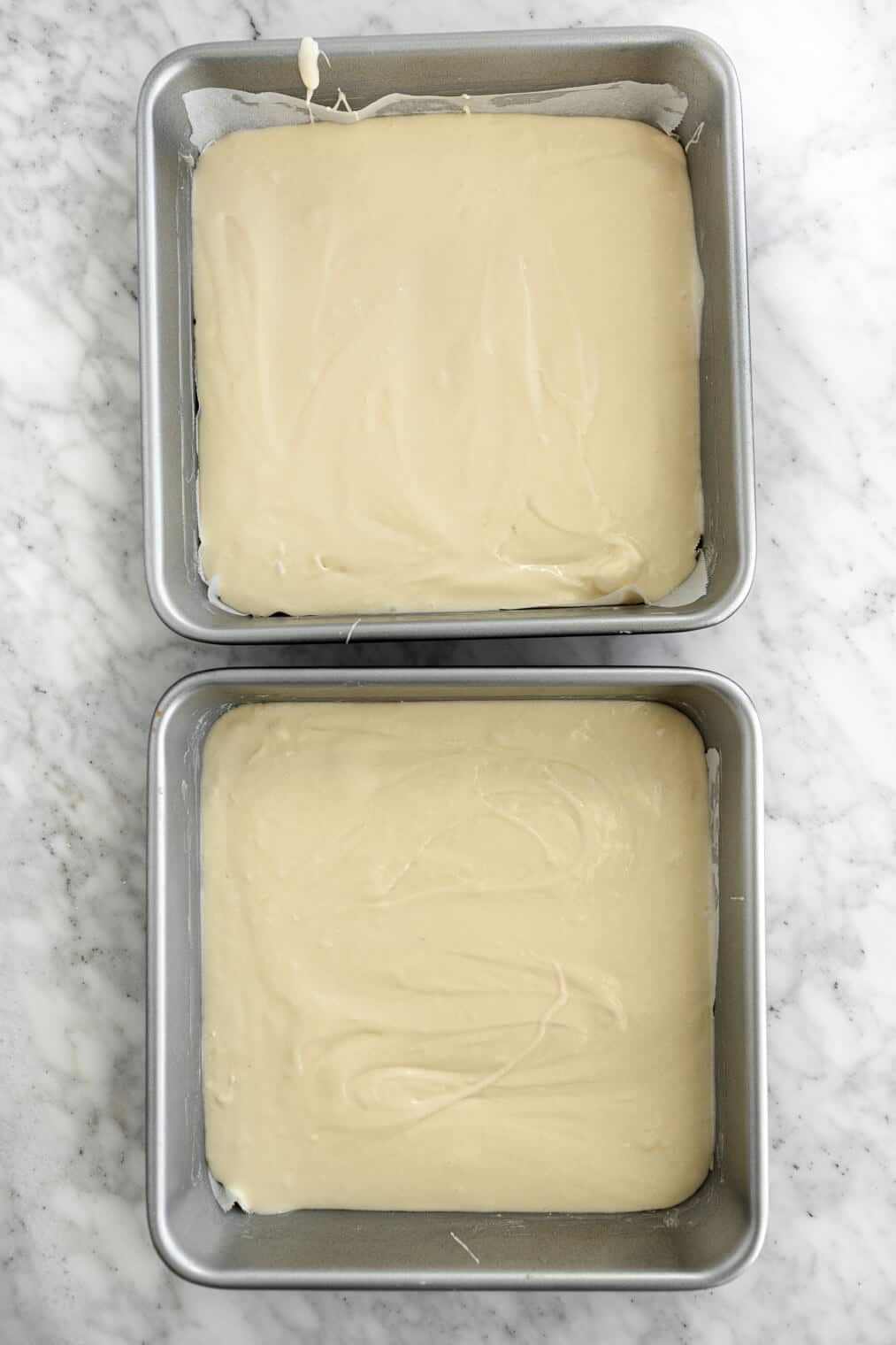 Cake mix in two square cake pans on a grey and white marble surface.
