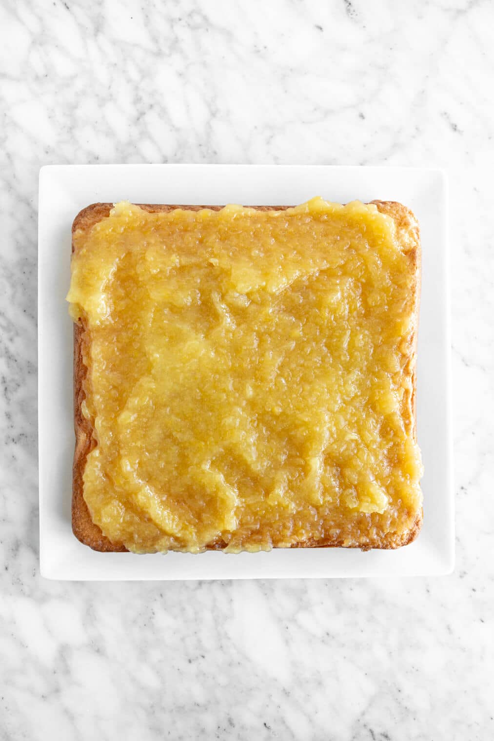 Square cake topped with pineapple filling on a white serving plate.