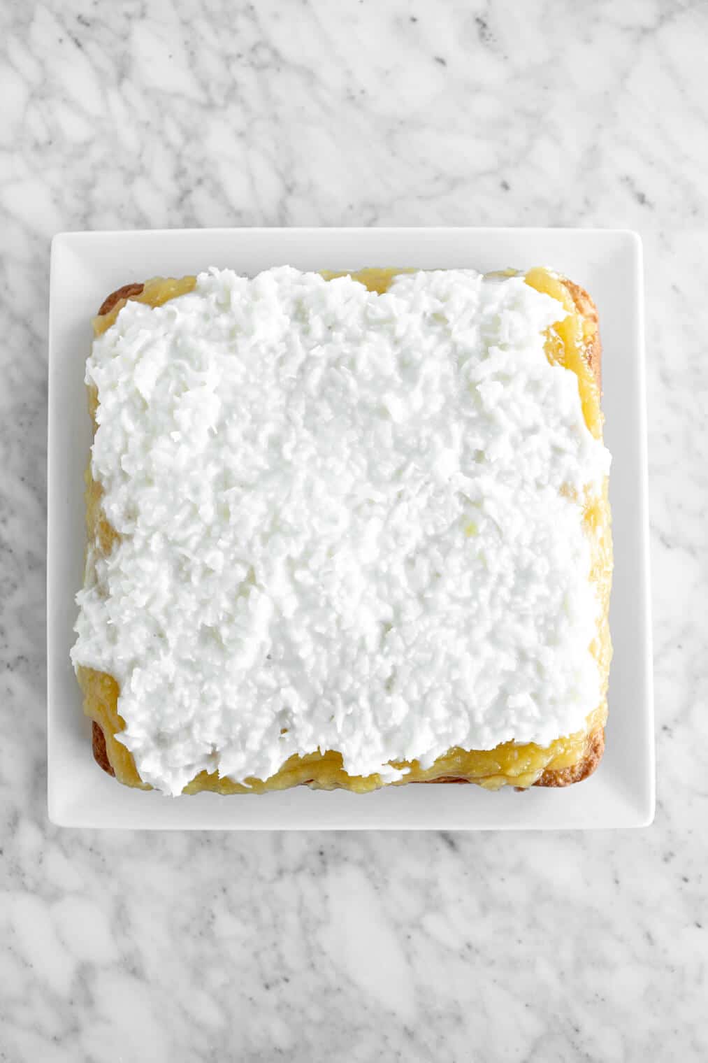 Square cake topped with coconut filling on a white serving plate.