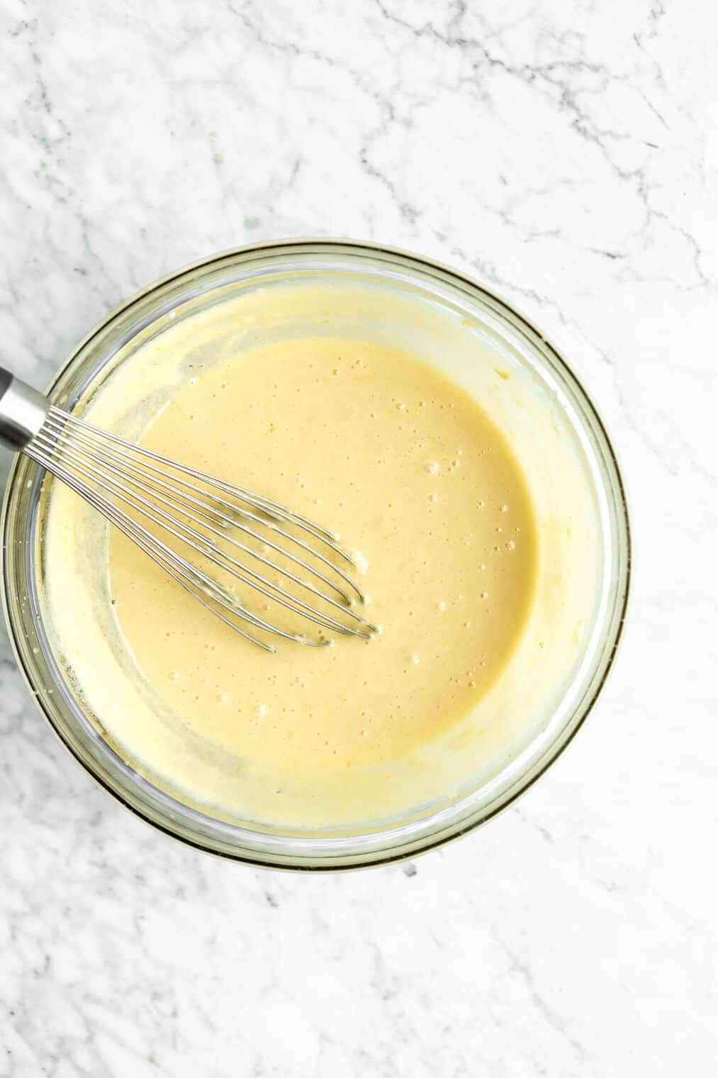 Lemon curd in glass bowl with a whisk.