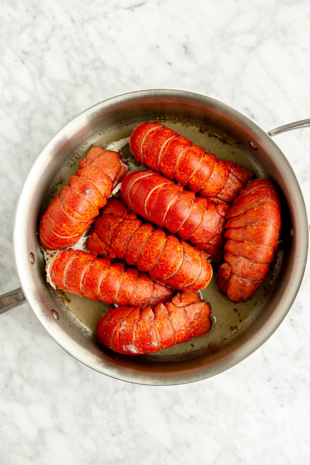Seven bright red lobster tails boiling in a white wine butter sauce.