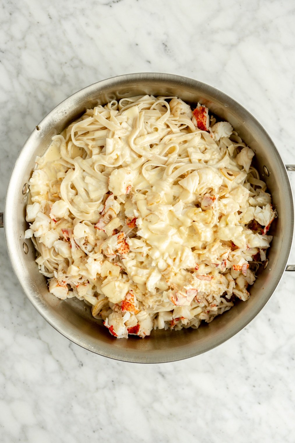 Fettuccine noodles, alfredo sauce, and chopped lobster in a large pan.