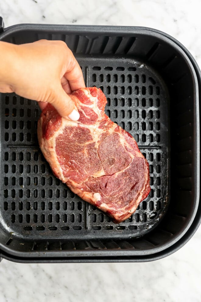 Steak being placed in an air fryer basket.