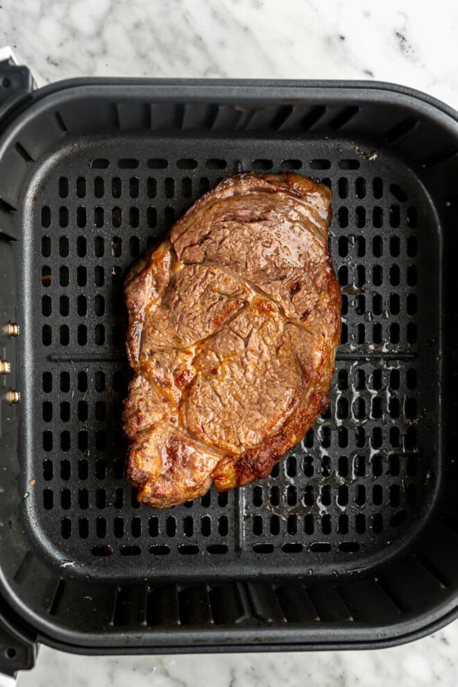 Cooked steak in an air fryer basket.