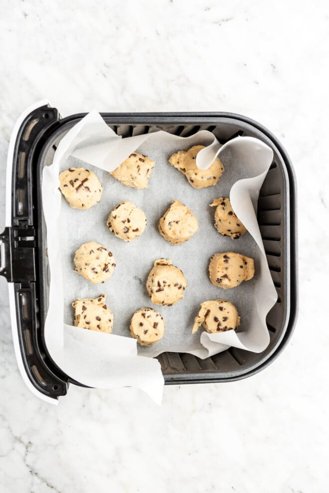 Air fryer basket lined with parchment paper filled with cookie dough balls.