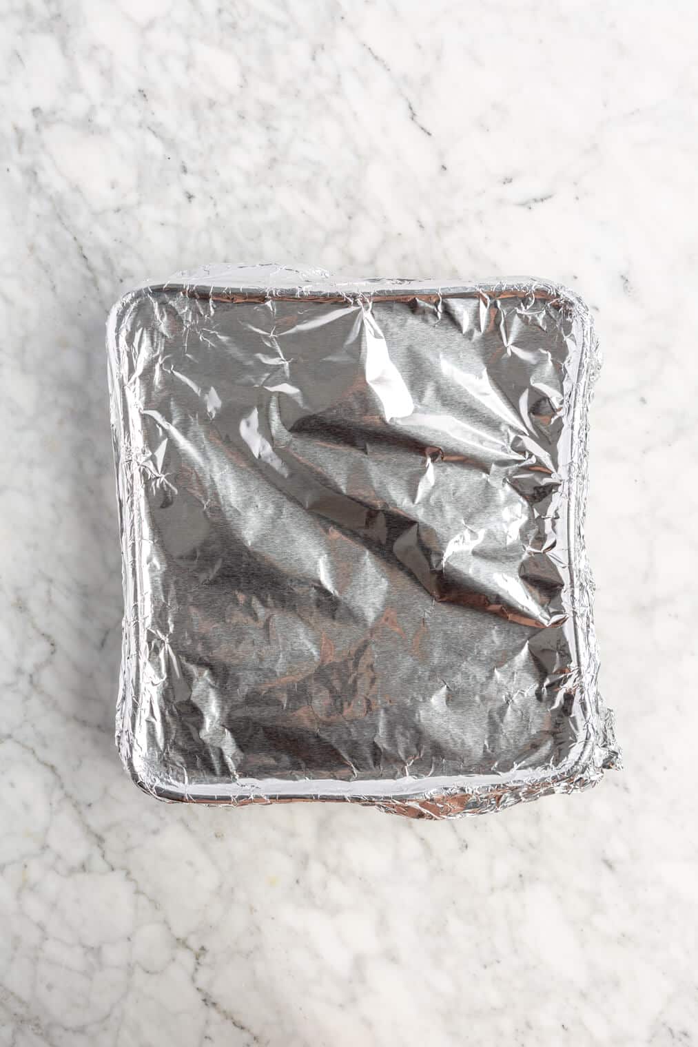 Casserole dish tightly covered with foil on a grey and white marble surface.