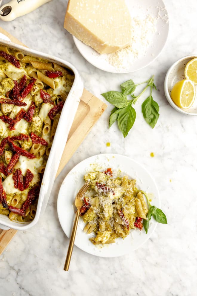 Plate of pesto pasta bake on a white plate next to casserole dish with pasta bake.