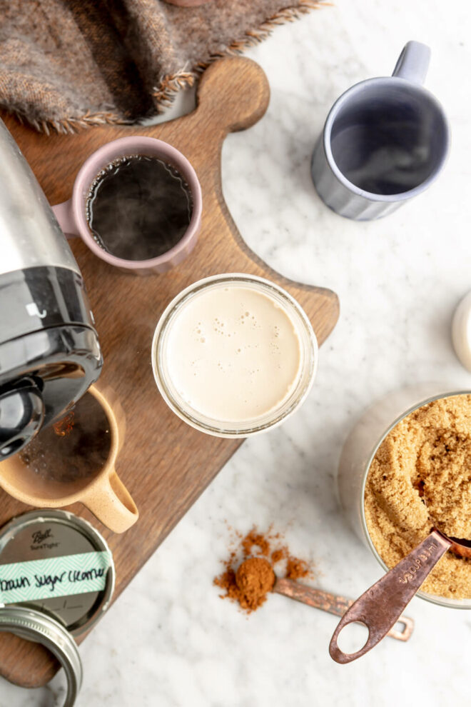 top down view of brown sugar creamer, creamer ingredients, and coffee mugs on a wooden cutting board on a gray and white marble surface