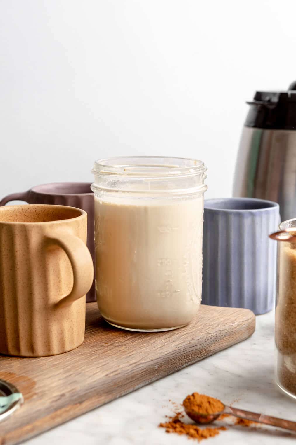 mason jar with brown sugar creamer on a wooden cutting board surrounded by coffee mugs.