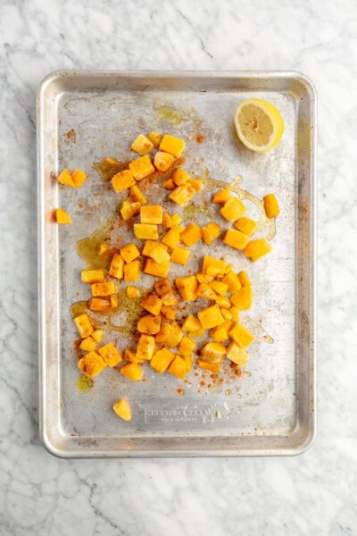 Frozen butternut squash on a sheet pan with a squeezed lemon next to it.
