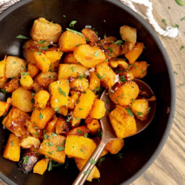 Black bowl with roasted butternut squash garnished with fresh herbs.