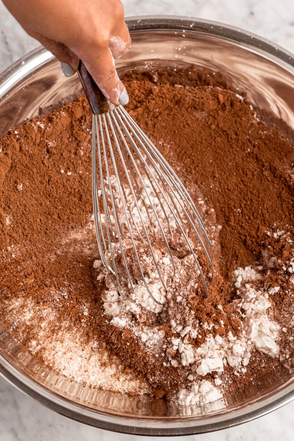 Dry chocolate cake ingredients being whisked together in a large, metal bowl.