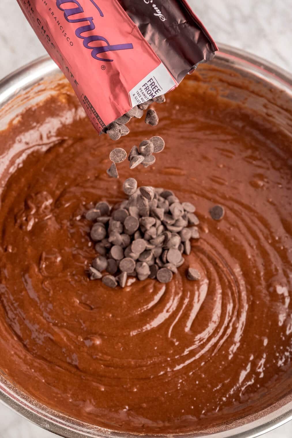 Chocolate chips being poured into chocolate cake batter.