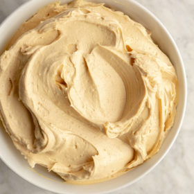 White bowl with peanut butter buttercream swirled inside on a beige marble surface.