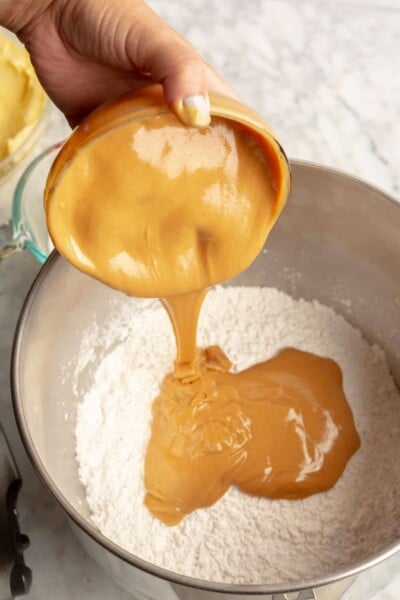 Hand pouring peanut butter into mixing bowl with powdered sugar.