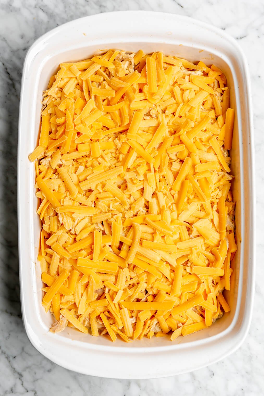Cheese spread on top of filling in a white casserole dish.