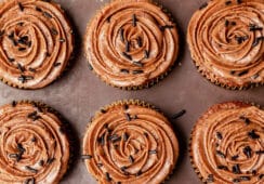 Top down view of 12 chocolate cupcakes topped with chocolate buttercream frosting swirled on top with chocolate sprinkles.