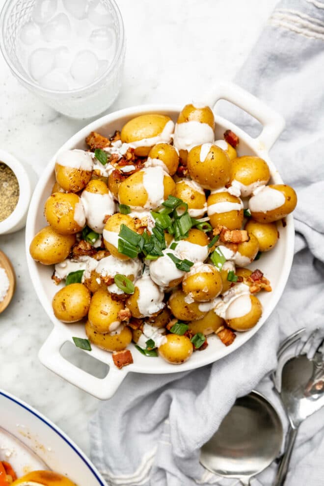 White serving dish with whole Yukon gold potatoes drizzled with a white sauce and garnished with green onions. 