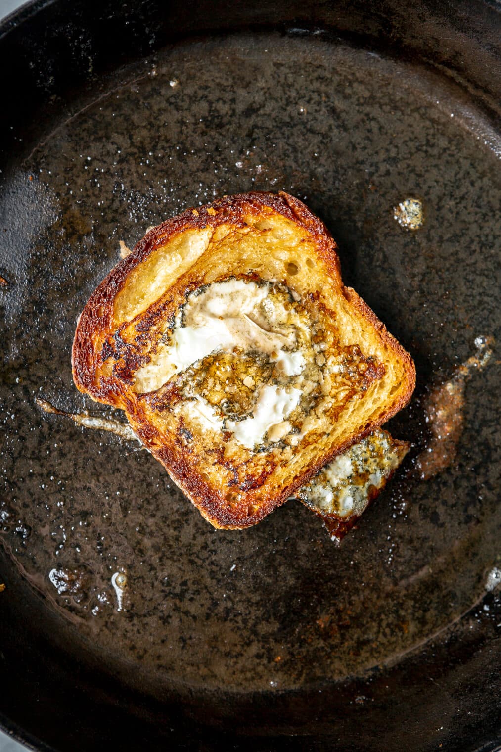 Slice of bread with egg cooked in the middle of the piece of bread in a cast iron skillet.