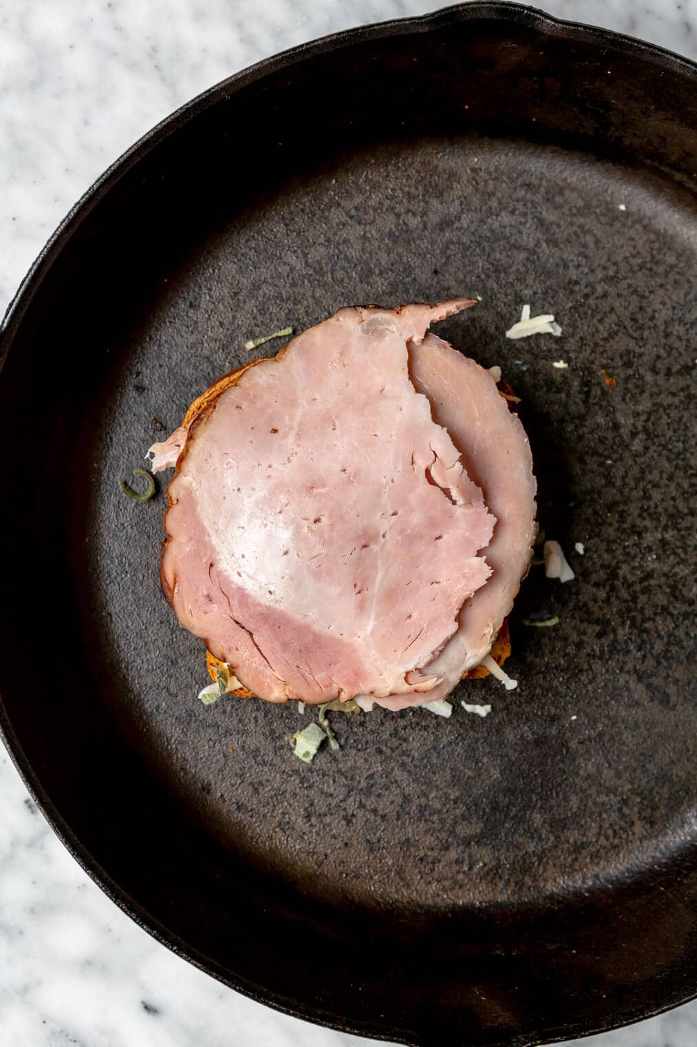 Ham on top of a piece of bread in a cast iron skillet.