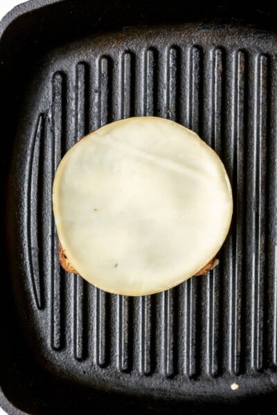 Slice of cheese on top of a slice of bread in a cast iron grill pan.