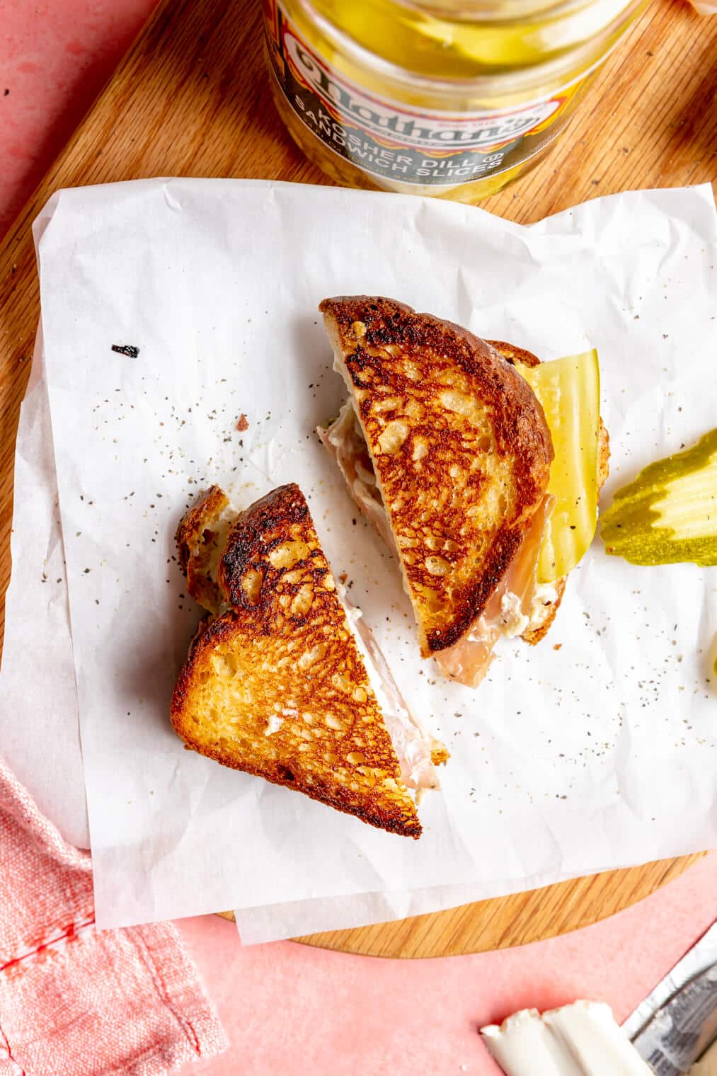 Sliced grilled cheese sandwich on a piece of white parchment paper with slice of pickle.