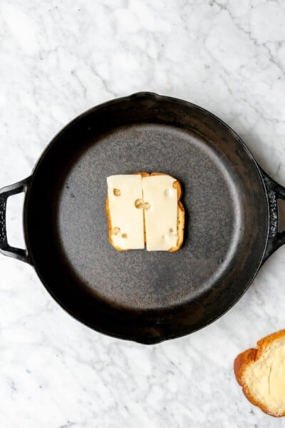 Slice of bread with Swiss cheese on top in a cast iron skillet.