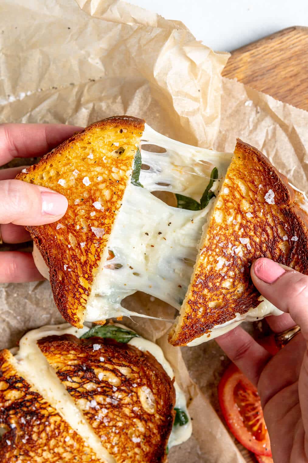 Two hands stretching grilled cheese sandwich with cheese pull connecting the two halves.