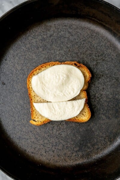 Slice of bread with mozzarella on top in a cast iron skillet.