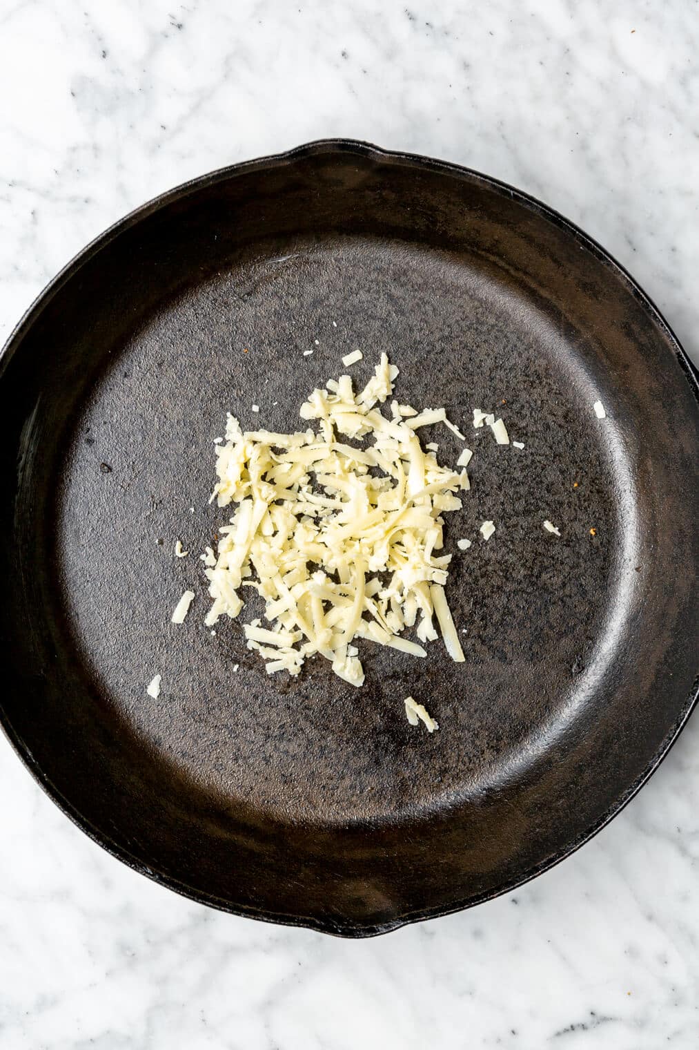 Shredded cheese sprinkled in a black, cast iron pan.
