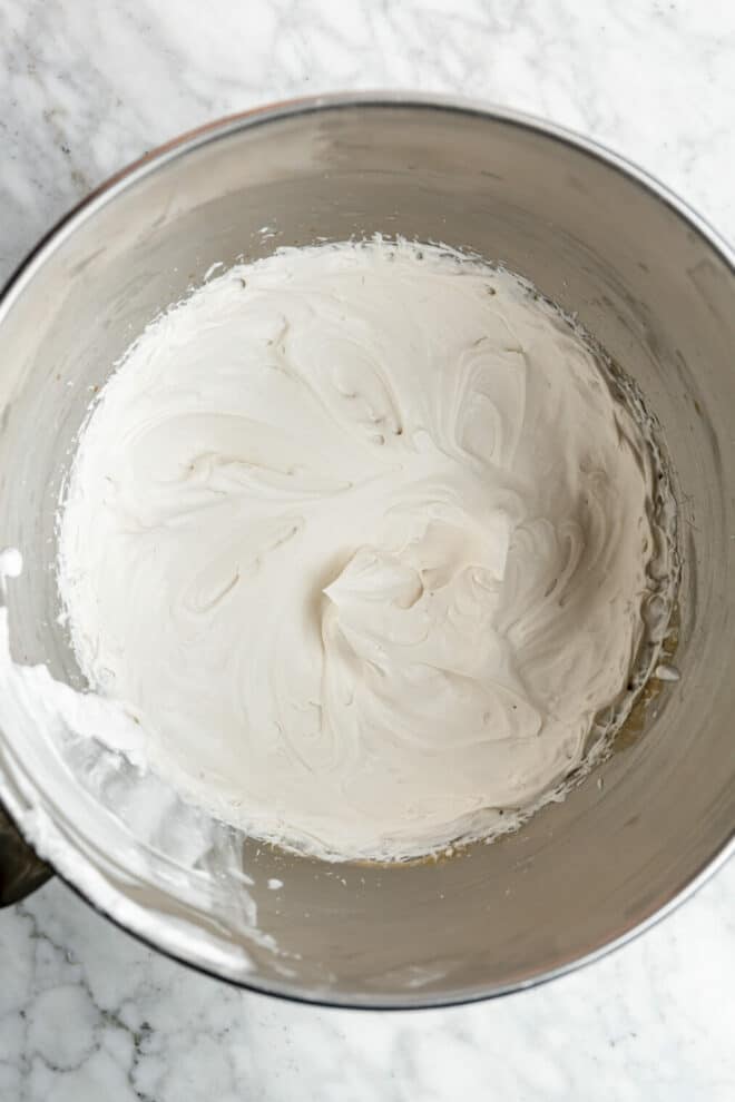 Whipped coconut milk in a large mixing bowl on a grey and white marble surface.