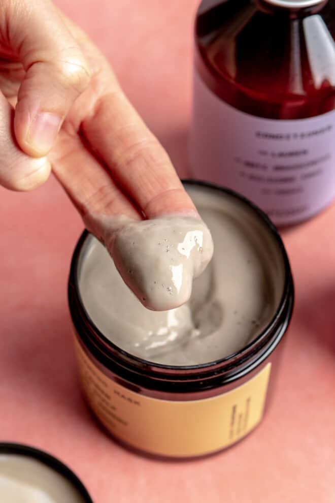 Hand with two fingers scooping hair mask out of container.